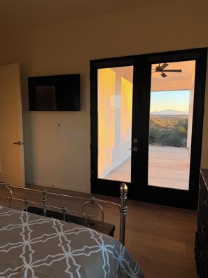 A bedroom with a bed, a TV mounted on the wall, and a door leading to a balcony with a view of a desert landscape. - New Private Desert Escape, Mtn Views with AC in sunny Tucson (Tucson)