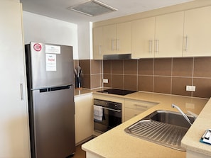 Eine kompakte Küche mit Edelstahl-Kühlschrank, einem eingebauten Backofen, einer Spüle mit modernem Wasserhahn und beigen Schränken.