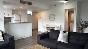 Ein modernes Wohnzimmer mit einer schwarzen Couch, einem kleinen Couchtisch und einem Essbereich mit weißem Tisch und Stühlen.
