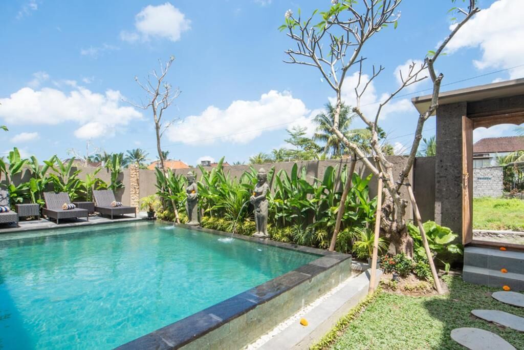 A swimming pool with lounge chairs, surrounded by greenery and a clear sky.