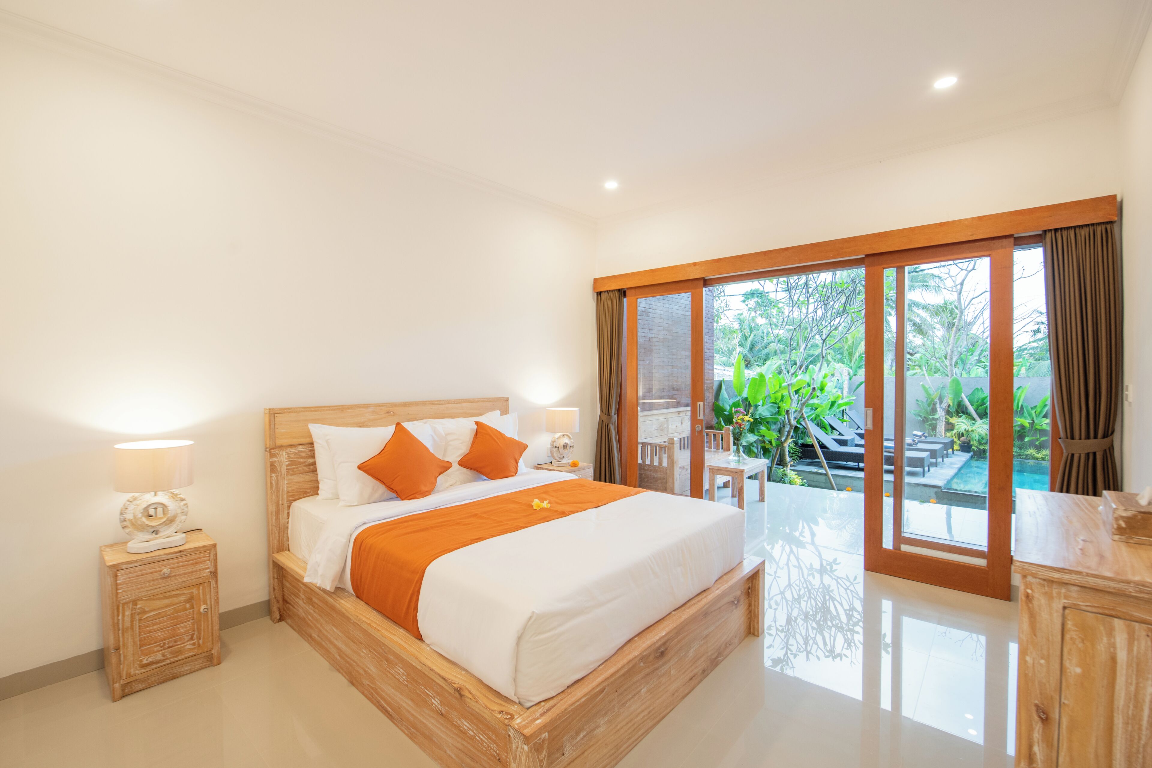 A bedroom with a wooden bed, a nightstand, a lamp, and a view of an outdoor pool area.