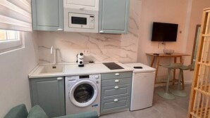 A compact kitchen with a washing machine, microwave, and a small dining area with a TV. - Baélia Casa Íbera Mini Apartment - Altamare (Alicante/Alacant)