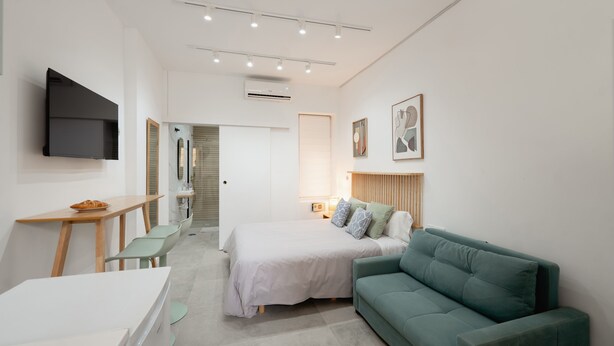 A modern hotel room with a bed, a green sofa, a desk, and a flat-screen TV. - Baélia Casa Íbera Mini Apartment - Altamare (Alicante/Alacant)
