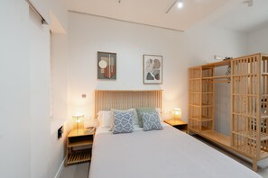 A bedroom with a bed, bedside lamps, a wooden wardrobe, and two framed artworks on the wall. - Mini Apartment Baélia Casa Íbera (Alicante/Alacant)