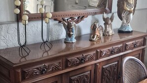 Uma cômoda de madeira com detalhes entalhados, um espelho grande e estátuas decorativas de anjos.