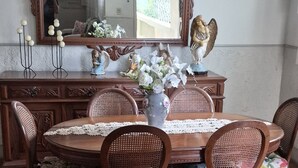 Uma sala de jantar com piso de madeira em padrão herringbone, uma mesa redonda com cadeiras, um espelho grande e um lustre.