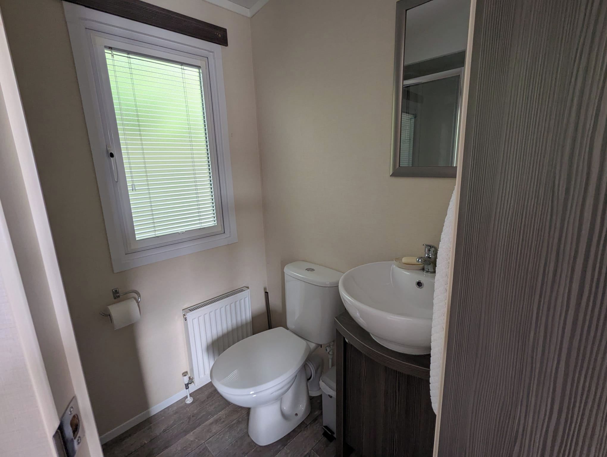 A small bathroom with a toilet, a sink, a window, and a radiator.