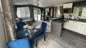 A compact RV interior with a dining area, kitchenette, and a sliding door to an outdoor deck. - Forest Retreat Cabin in Ringwood (Ringwood)