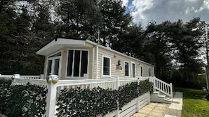 A single-story mobile home with a covered porch, surrounded by dense trees and a stone pathway. - Forest Retreat Cabin in Ringwood (Ringwood)