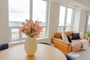 Une pièce avec une table ronde, un vase de fleurs, un canapé et de grandes fenêtres.