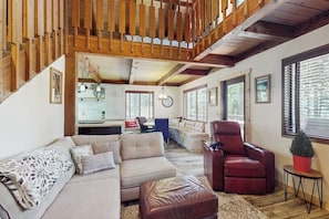 Amplia sala de estar con techo alto, vigas de madera, un juego de sofás, un sillón de cuero y una pequeña mesa con una planta.