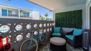 En balkon med cykel, fletmøbler og en væg med grønne planter.