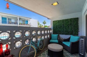 Ein Balkon mit einem Fahrrad, Korbmöbeln und einer mit Grünpflanzen bepflanzten Wand.