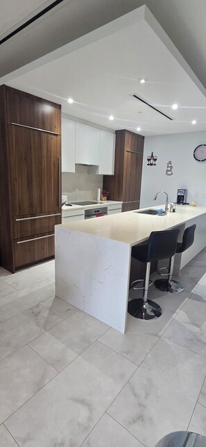 A modern kitchen with a marble island, wooden cabinets, and bar stools. - Paradise at one cable beach (Nassau)