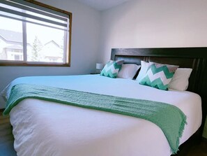 Un lit bien fait, avec une couverture verte, une tête de lit en bois et une fenêtre équipée de stores.