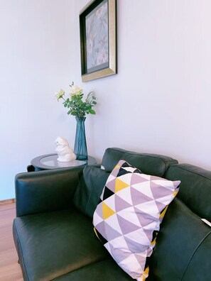 A dark green sofa with a geometric-patterned pillow, a small white statue, and a vase with flowers on a side table. - Modern 3BR Panorama Home | Garage | Near YYC (Calgary)