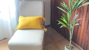 A room with a white armchair, a yellow pillow, and a potted plant.