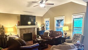 A living room with a fireplace, leather sofas, a ceiling fan, and a television. - Luxury Golf Course Chalet Near World Cup Matches Airport and Legends, Sleeps 6+ (Basehor)