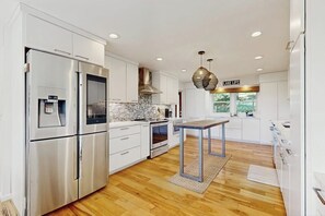 A modern kitchen with stainless steel appliances, a marble backsplash, and a central island. - Stunning home with amazing views, a private pool, serenity & lake access (Meredith)