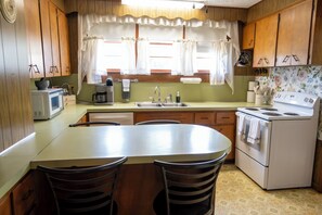 Une cuisine avec des meubles de rangement en bois, un fourneau blanc, un évier et une table à manger avec des chaises.