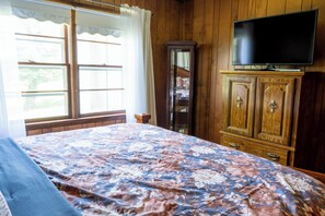 Een kamer met een bed, een televisie op een kast en een raam met gordijnen.