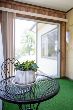 Een ronde metalen tafel met een witte pot groene planten, een zwarte metalen stoel en een schuifdeur naar buiten.