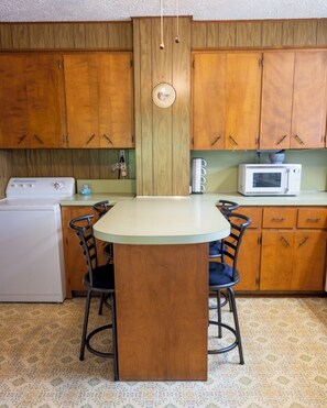 Een keuken met houten kastjes, een witte oven, een magnetron en een ronde tafel met stoelen.
