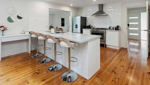 A modern kitchen with a central island, bar stools, a stove, and a large window. - Foreshore Hideaway - Capel Sound (Capel Sound)