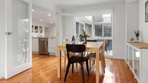A modern kitchen with white cabinets, a dishwasher, and a dining area with a wooden table and chairs. - Foreshore Hideaway - Capel Sound (Capel Sound)