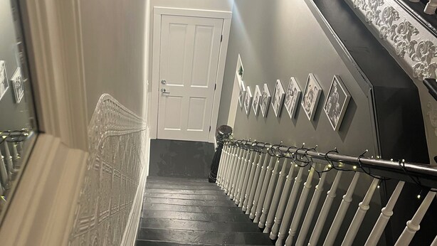 Una escalera con barandilla, una puerta arriba y cuadros en la pared.