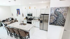 Een moderne keuken met witte kasten, een centraal eiland, roestvrijstalen apparatuur en een decoratief pauwen schilderij.