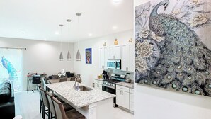 Een moderne keuken met witte kasten, een centraal eiland en een pauwschilderij aan de muur.