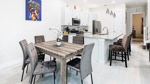 Een moderne keuken met witte kasten, roestvrijstalen apparatuur en een houten eettafel met gestoffeerde stoelen.