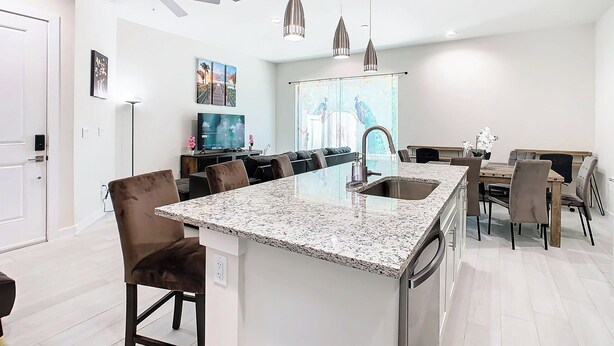 Een moderne keuken met een centraal eiland, barkrukken, een eethoek en een plafondventilator.