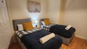 A room with two beds, each with a checkered blanket and a pillow. There is a painting on the wall above the beds. - Comfy 3-bed House - Sleeps 6 & Free Parking (Tilbury)