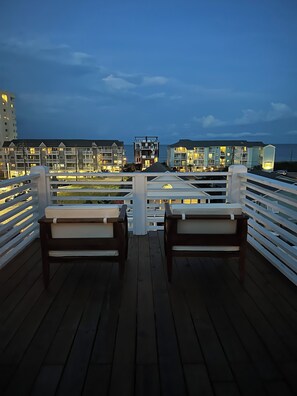 Eine Terrasse mit zwei Holzstühlen, einem Geländer und Gebäuden im Hintergrund.