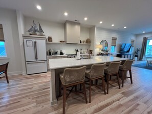 Uma cozinha moderna com ilha central, eletrodomésticos embutidos e um espaço de jantar com cadeiras de vime.