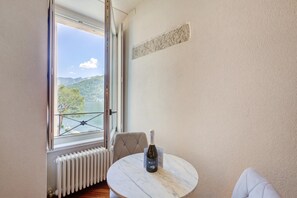 Una habitación con vistas a un lago y montañas, un radiador blanco, una mesa redonda con una botella y una silla.