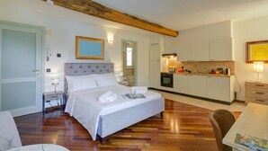 A bedroom with a large bed, a bedside table, a nightstand, a wooden ceiling beam, a small kitchen area, and a dining table. - Historic Palazzo Gritti - Lugano Lakefront stay - Fiordaliso, Morcote, Switzerland (Morcote)