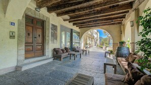 Zona relax esterna con pavimento in pietra, arredi in legno e vista attraverso un arco.