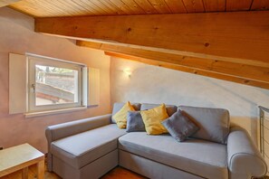 Un canapé d’angle avec des coussins, un plafond en bois, une fenêtre et un luminaire fixé au mur.