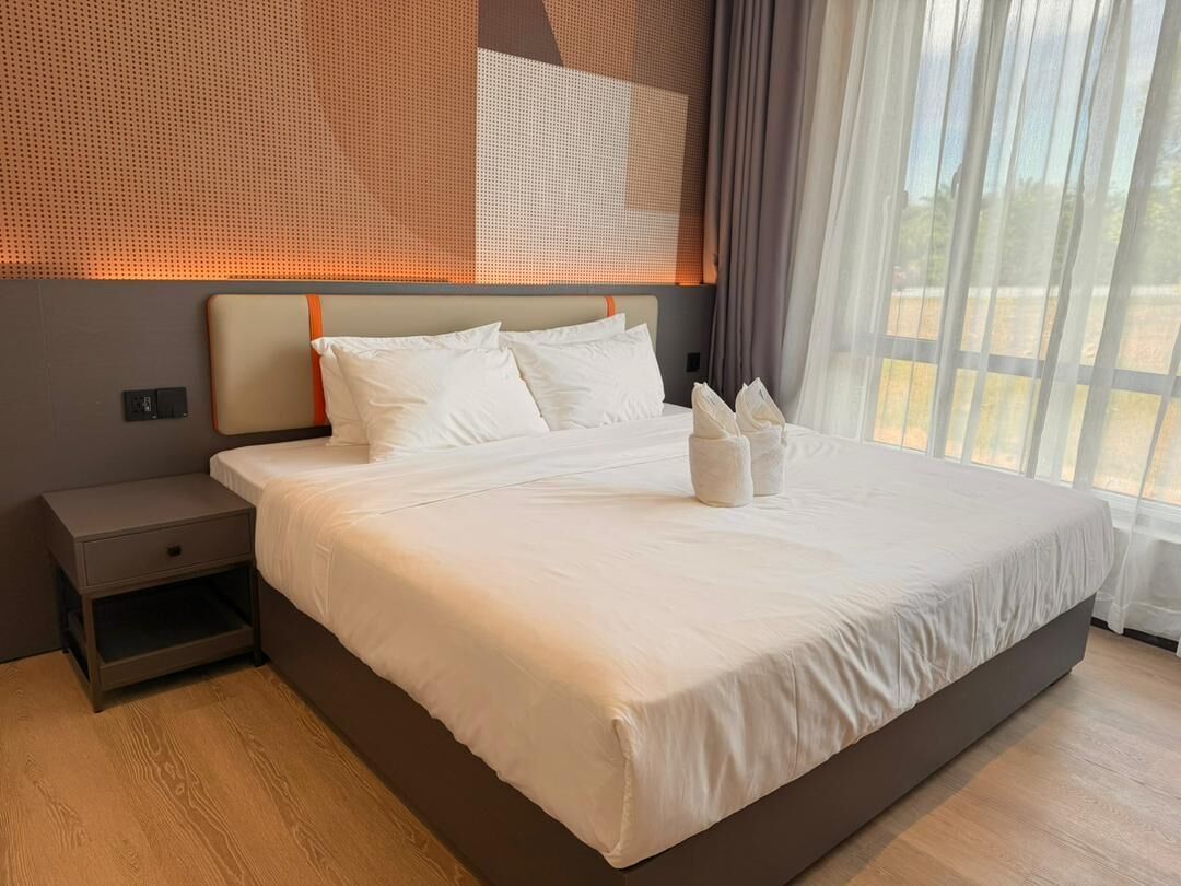 Una cama grande con sábanas blancas, una mesita de noche y una ventana con cortinas.