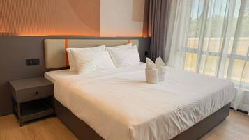 Una cama grande con sábanas blancas, una mesita de noche y una ventana con cortinas.