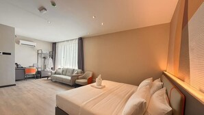 Ett hotellrum med en säng, ett skrivbord, en stol, en soffa och ett fönster med gardiner.