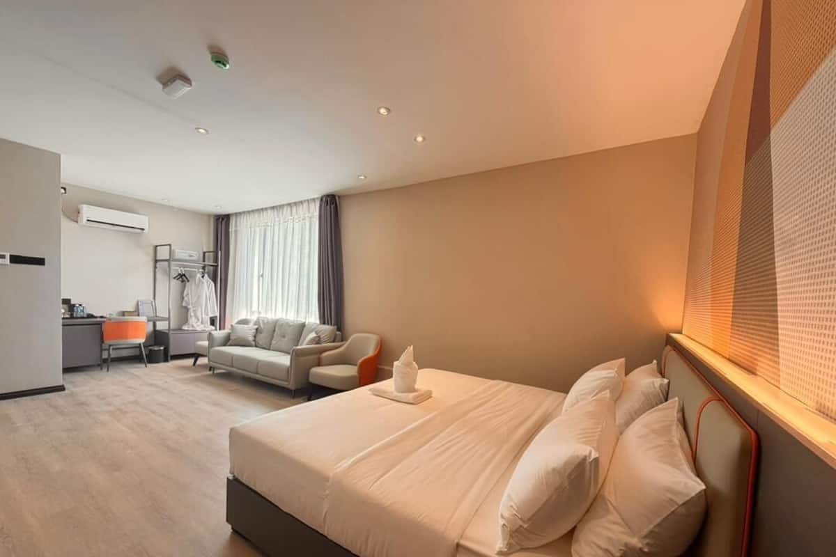 A hotel room with a bed, a desk, a chair, a sofa, and a window with curtains.