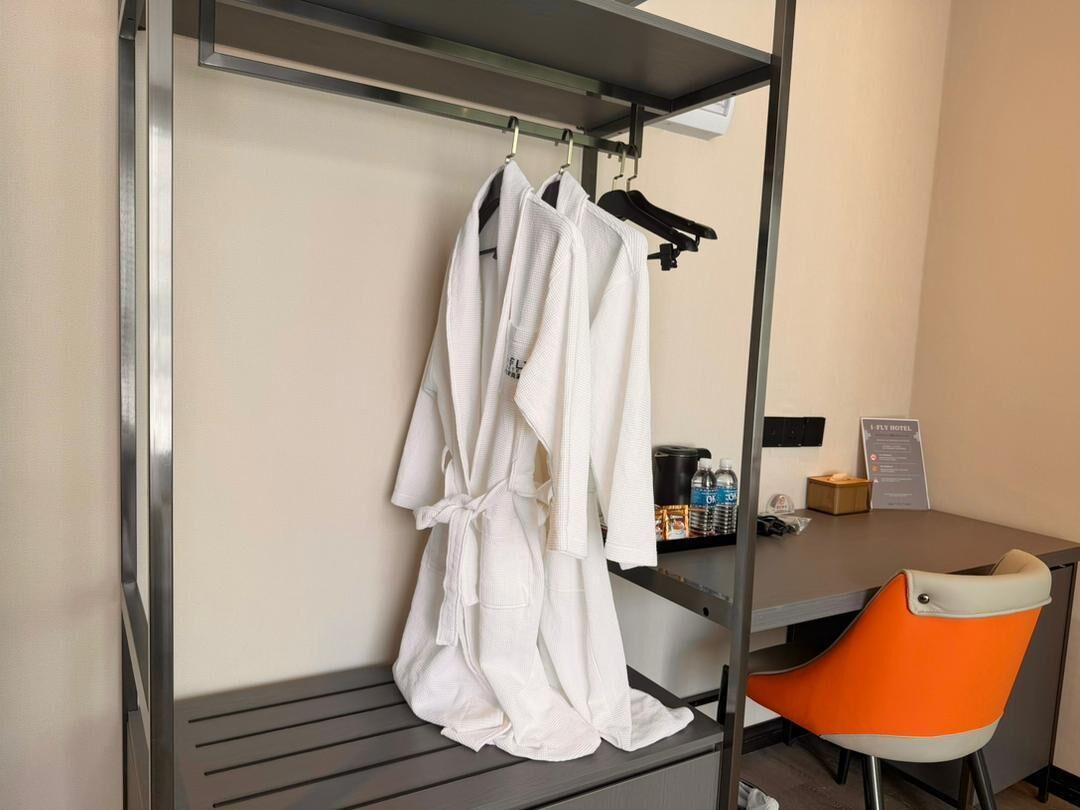 Une chambre d’hôtel avec un lit, un bureau, une chaise et un peignoir suspendu à un porte-manteau.