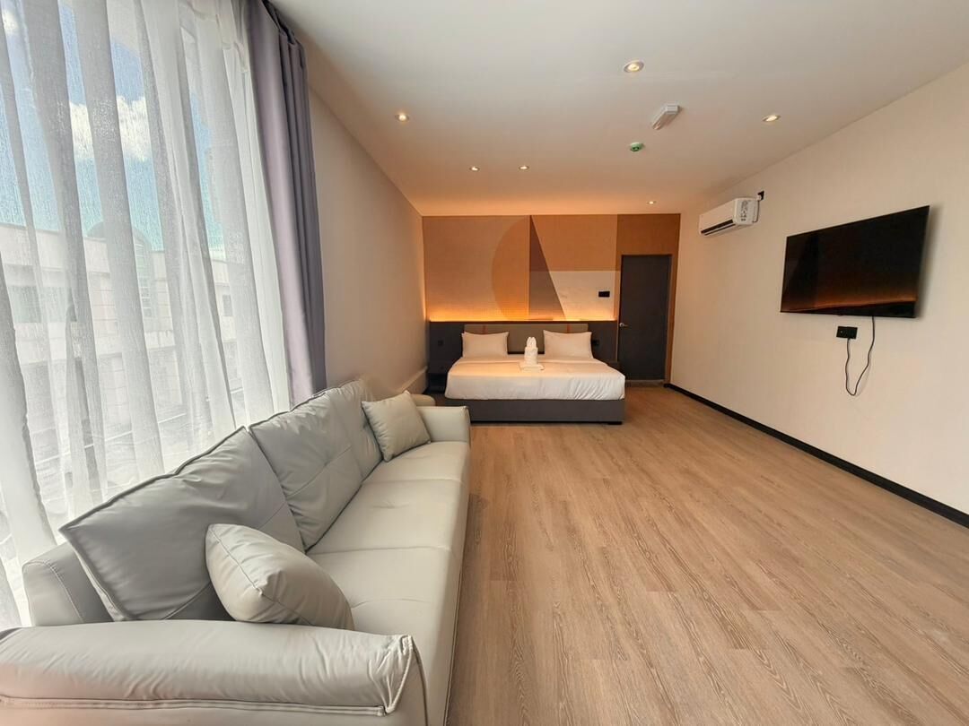 A modern hotel room with a bed, a sofa, a flat-screen TV, and a large window with curtains.