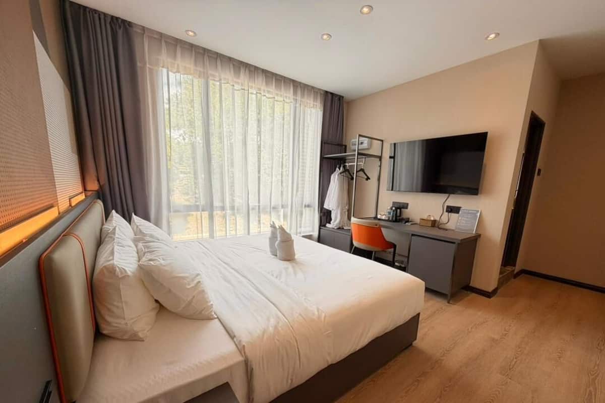A modern hotel room with a large bed, a desk, a chair, a TV, and a window with curtains.