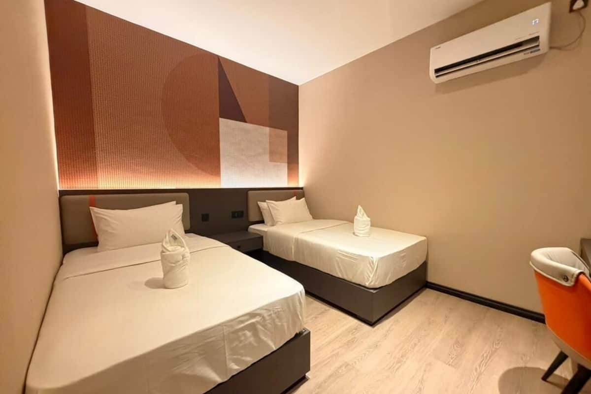 A hotel room with two beds, a wall-mounted air conditioner, and a wooden floor.
