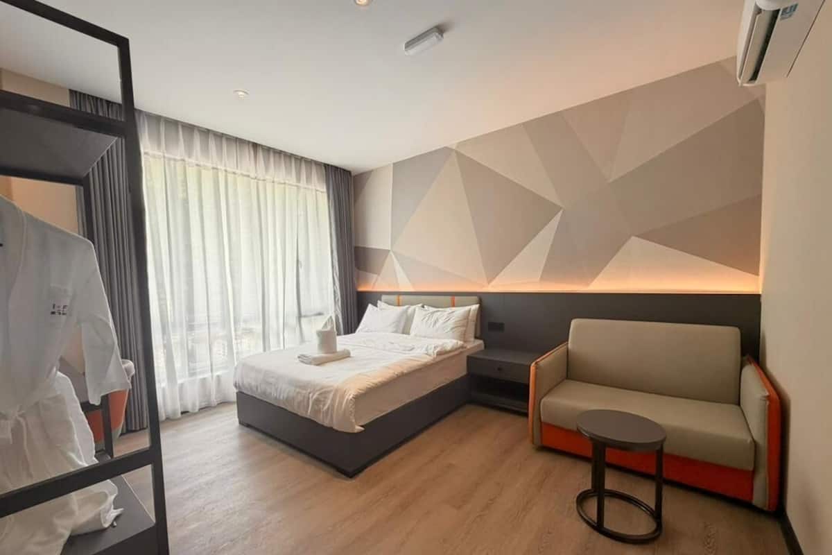 A modern hotel room with a bed, a sofa, a small table, and a mirror.